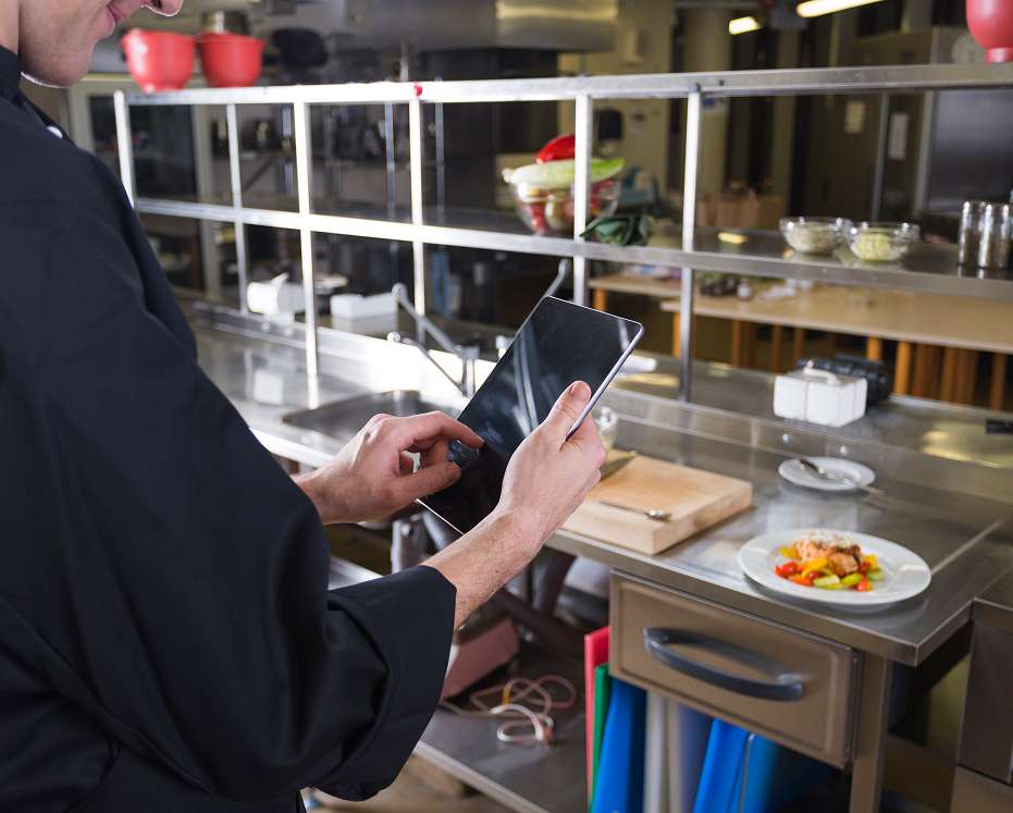 Staff member using a tablet in a commercial kitchen for canteen management system operations.