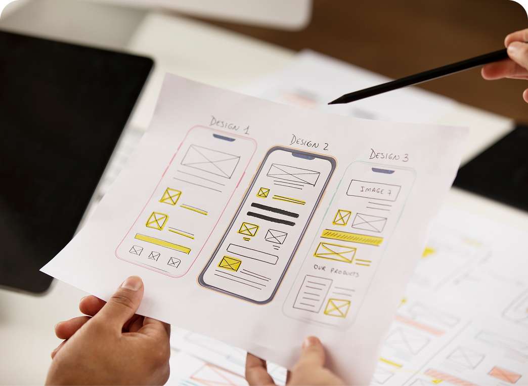 Printed UX/UI wireframe layouts being reviewed during a web design project at an IT services company.