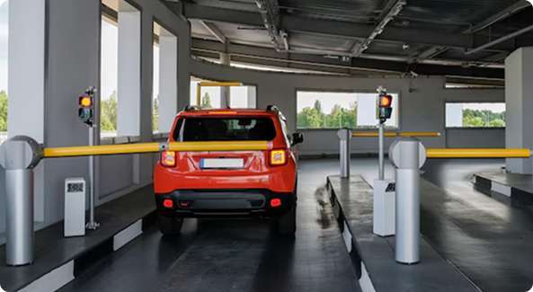 Automated Vehicle Parking Solutions: A small red car is stopped at a yellow parking barrier in an indoor parking facility.