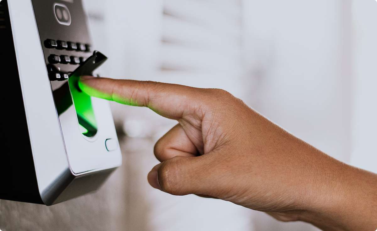 Close-up of a person scanning their fingerprint on a biometric time and attendance device mounted on a wall.