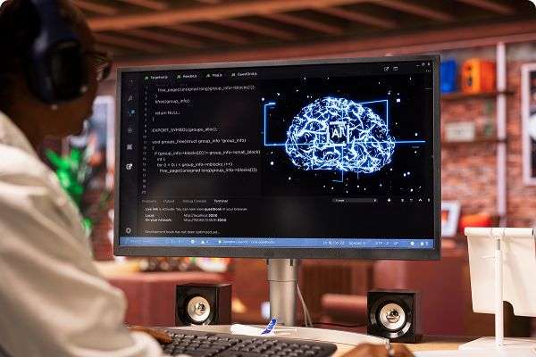 A person working at a computer displaying AI code and a digital brain interface on the screen, representing artificial intelligence technology.